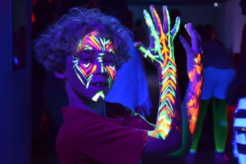 A boy with glow-in-the-dark paints on his face and arms